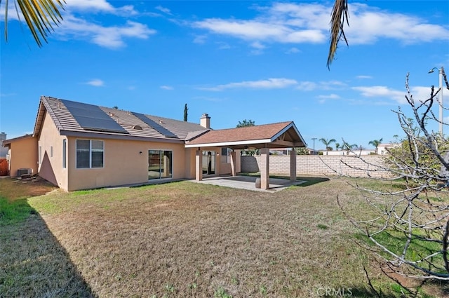 rear view of house with a patio, solar panels, stucco siding, a lawn, and fence