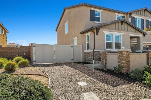 rear view of house with stone siding, a gate, fence, and stucco siding