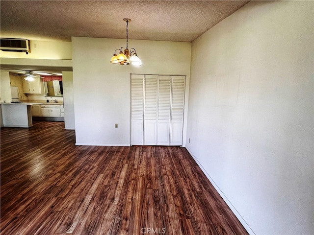 unfurnished dining area with a textured ceiling, ceiling fan with notable chandelier, dark wood-style flooring, a sink, and baseboards