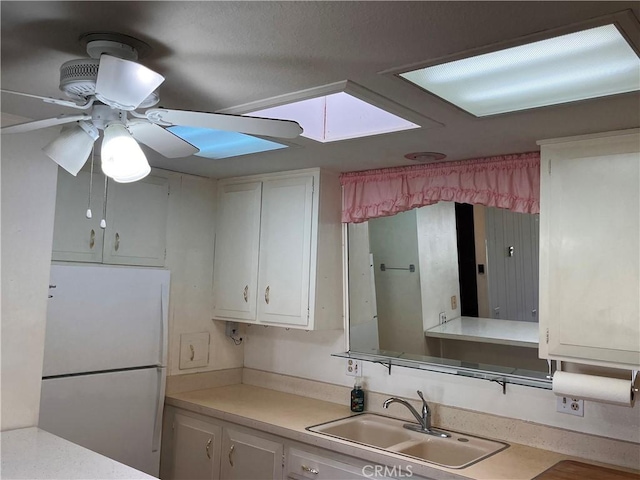 kitchen featuring light countertops, freestanding refrigerator, white cabinets, and a sink