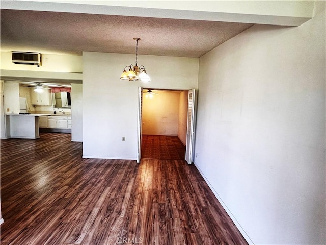 unfurnished dining area with baseboards, dark wood-type flooring, a textured ceiling, a sink, and ceiling fan with notable chandelier