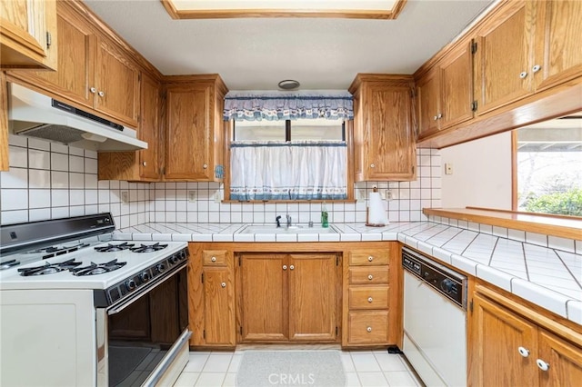 kitchen with brown cabinets, dishwasher, under cabinet range hood, and gas range