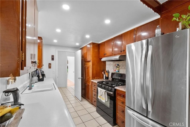 kitchen featuring light tile patterned floors, black gas range, under cabinet range hood, light countertops, and freestanding refrigerator