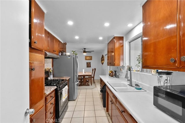 kitchen featuring light countertops, light tile patterned flooring, a sink, under cabinet range hood, and black appliances