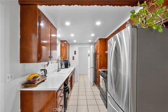 kitchen featuring black gas range, brown cabinetry, freestanding refrigerator, light countertops, and light tile patterned flooring