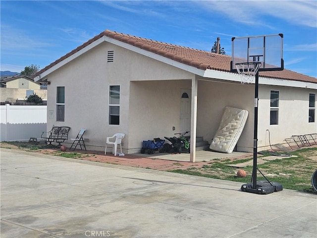 back of property featuring fence, a tiled roof, and stucco siding