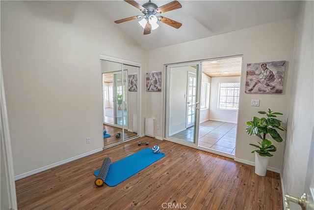 workout area featuring a ceiling fan, lofted ceiling, baseboards, and wood finished floors