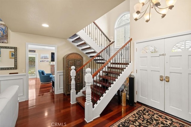 foyer entrance featuring a chandelier, a decorative wall, wood finished floors, stairway, and wainscoting