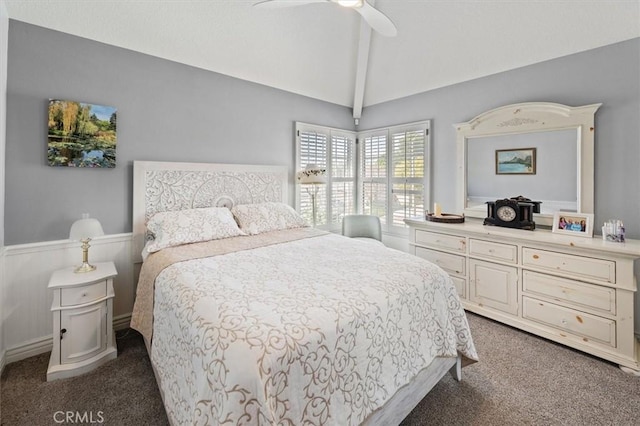 bedroom with a ceiling fan, dark colored carpet, wainscoting, and vaulted ceiling with beams