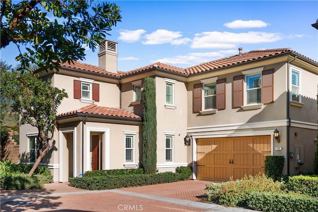 mediterranean / spanish home with a tiled roof, a chimney, decorative driveway, and stucco siding