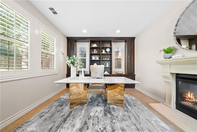 home office featuring light wood-style flooring, visible vents, baseboards, and a glass covered fireplace