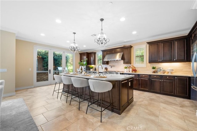 kitchen with a kitchen breakfast bar, light countertops, crown molding, under cabinet range hood, and backsplash