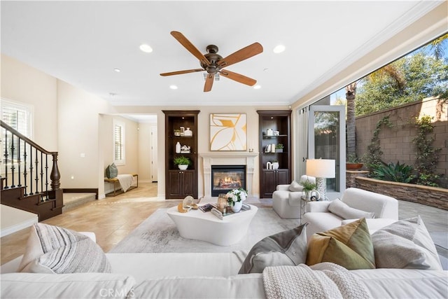 living area with recessed lighting, ornamental molding, a glass covered fireplace, baseboards, and stairs