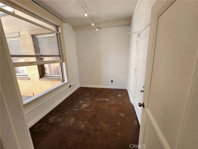 spare room featuring rail lighting and baseboards