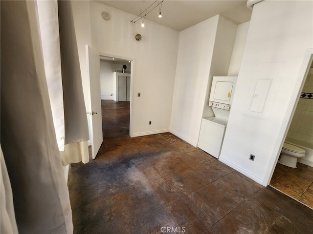 unfurnished bedroom with stone finish flooring, connected bathroom, baseboards, and stacked washer / dryer