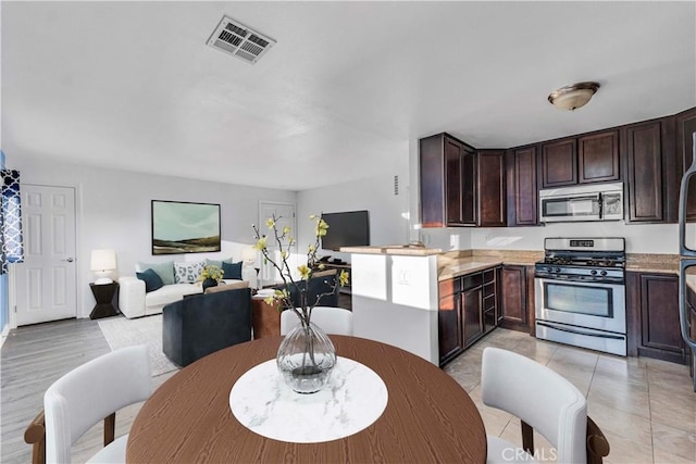 kitchen featuring visible vents, open floor plan, dark brown cabinets, appliances with stainless steel finishes, and light countertops