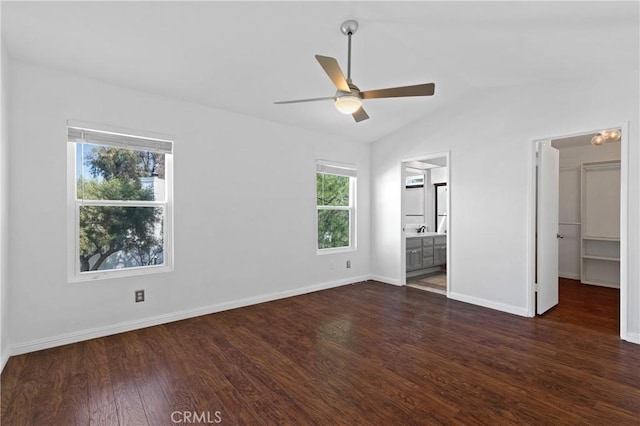 unfurnished bedroom featuring baseboards, dark wood-type flooring, ensuite bathroom, a spacious closet, and vaulted ceiling