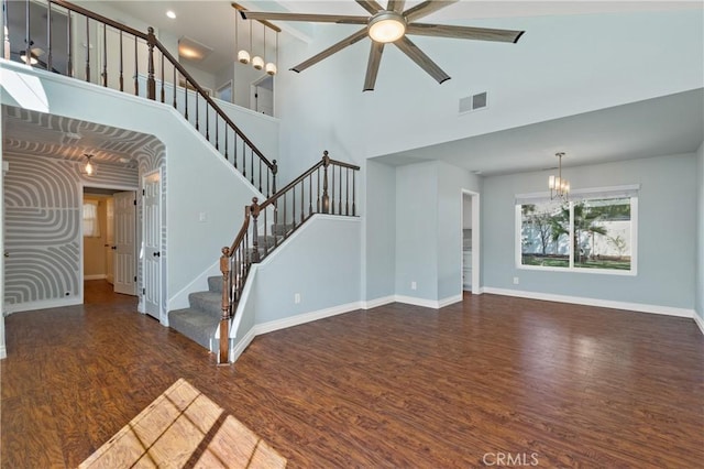 unfurnished living room with ceiling fan with notable chandelier, wood finished floors, visible vents, baseboards, and stairway