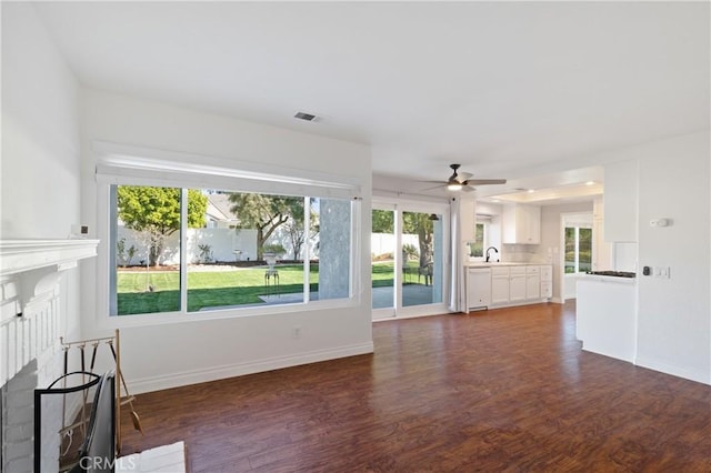 unfurnished living room with a fireplace, a sink, visible vents, plenty of natural light, and dark wood finished floors