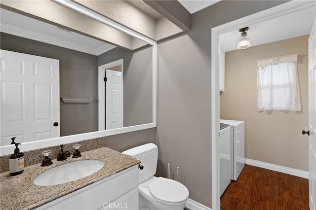 bathroom with baseboards, toilet, wood finished floors, washing machine and clothes dryer, and vanity