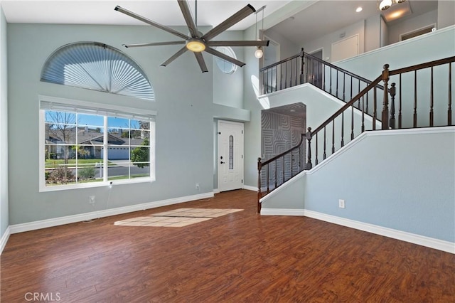 unfurnished living room featuring high vaulted ceiling, stairway, baseboards, and wood finished floors