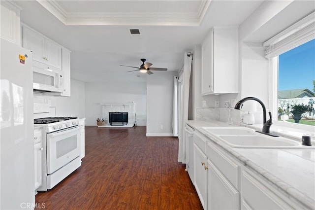 kitchen featuring a tray ceiling, visible vents, a brick fireplace, a sink, and white appliances