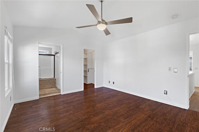 unfurnished bedroom with a closet, a spacious closet, vaulted ceiling, wood finished floors, and baseboards