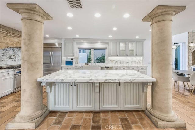 kitchen with visible vents, high end appliances, backsplash, and decorative columns