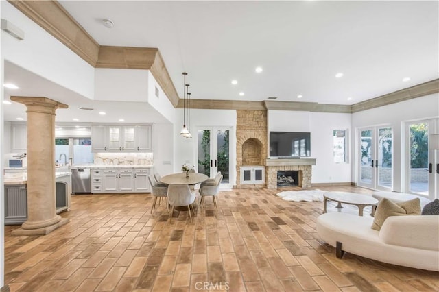 living area with decorative columns, ornamental molding, a stone fireplace, and french doors