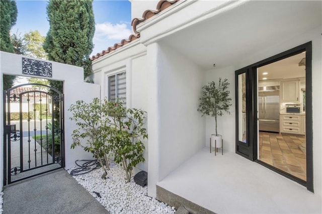 view of exterior entry with a tiled roof, a gate, and stucco siding