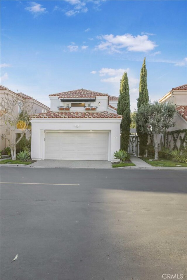 mediterranean / spanish house with stucco siding, an attached garage, a gate, driveway, and a tiled roof