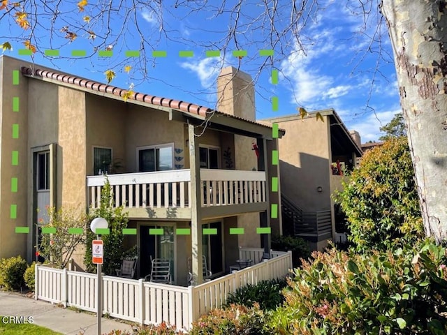 exterior space with a chimney, a balcony, and stucco siding