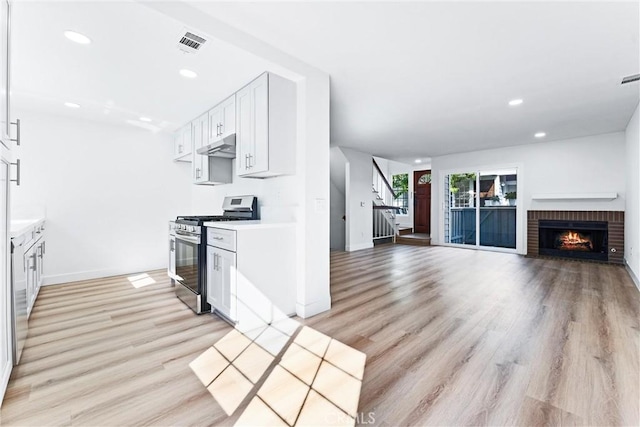 kitchen featuring light wood finished floors, stainless steel gas range oven, visible vents, under cabinet range hood, and recessed lighting