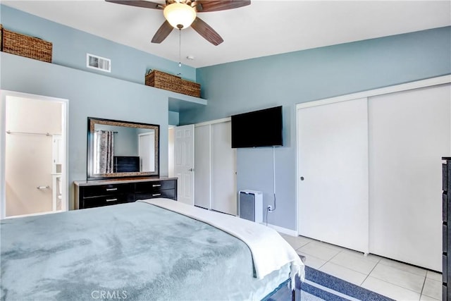 bedroom with light tile patterned flooring, a ceiling fan, visible vents, vaulted ceiling, and multiple closets