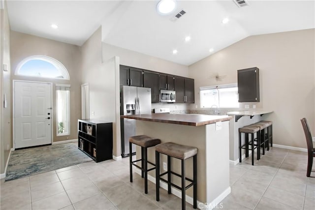 kitchen featuring a breakfast bar area, light tile patterned flooring, dark cabinets, stainless steel appliances, and visible vents