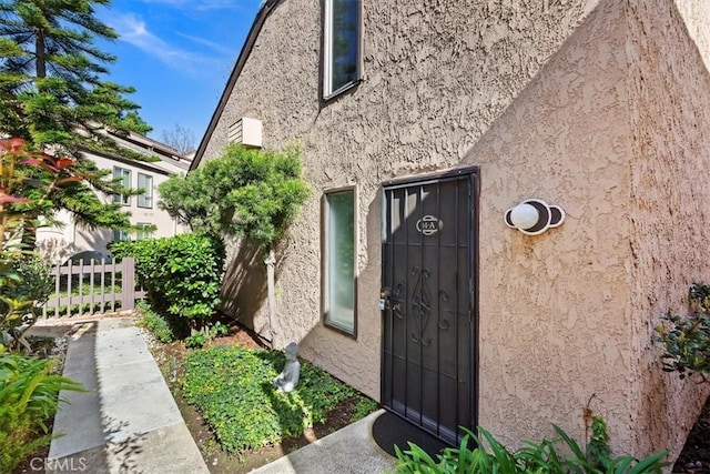 view of exterior entry featuring fence and stucco siding