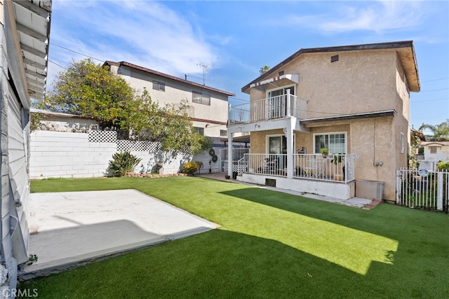 back of property featuring a fenced backyard, a lawn, a balcony, and stucco siding