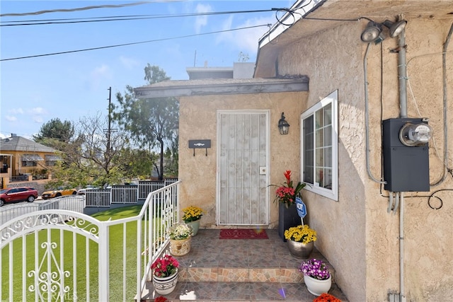 view of exterior entry featuring fence, a lawn, and stucco siding