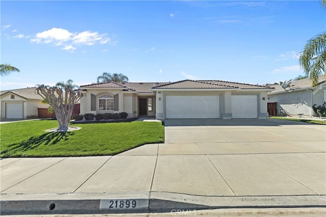 view of front facade with stucco siding, an attached garage, a front yard, driveway, and a tiled roof