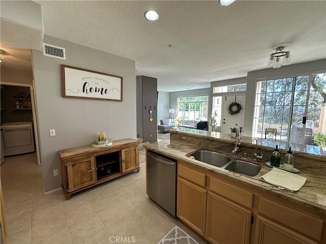 kitchen featuring a textured ceiling, a sink, visible vents, dishwasher, and washer / dryer