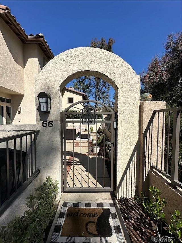 view of exterior entry featuring a gate, fence, a tiled roof, and stucco siding