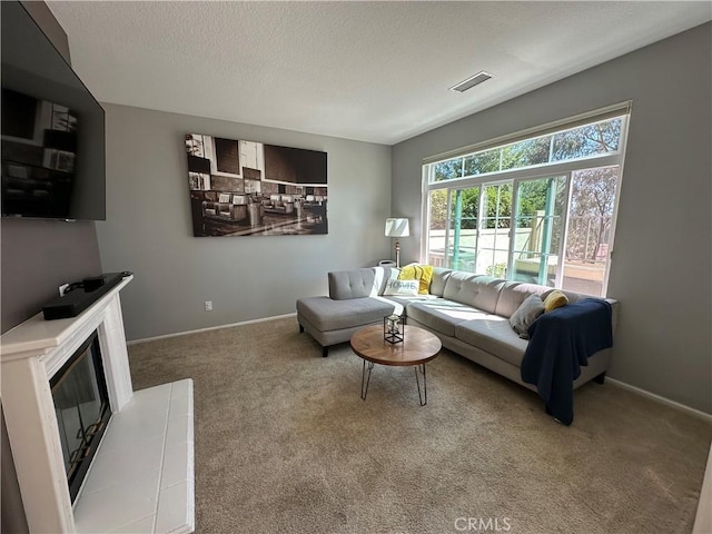 living room featuring visible vents, a glass covered fireplace, carpet flooring, a textured ceiling, and baseboards