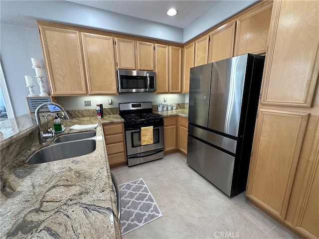 kitchen with light tile patterned floors, appliances with stainless steel finishes, light stone counters, light brown cabinetry, and a sink