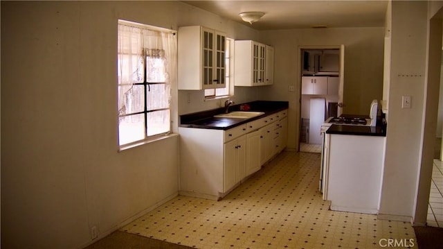 kitchen featuring range with gas stovetop, light floors, dark countertops, white cabinets, and a sink