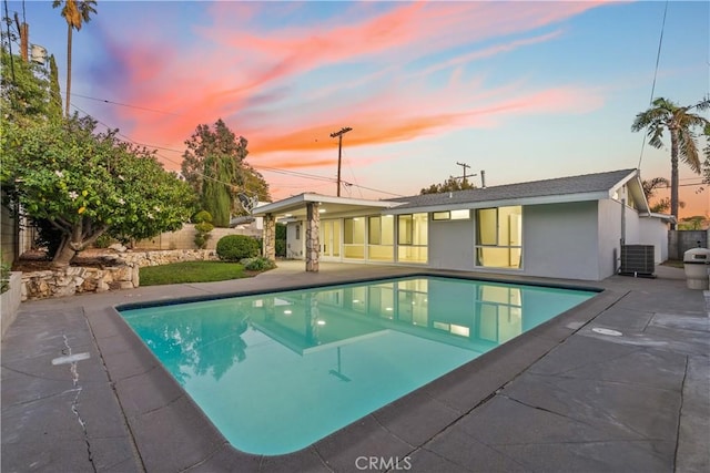 pool at dusk with a patio, fence, and central air condition unit