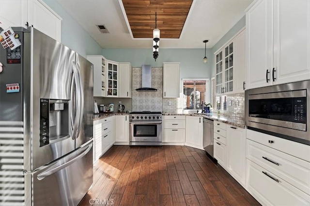 kitchen featuring stainless steel appliances, visible vents, wall chimney range hood, backsplash, and a raised ceiling