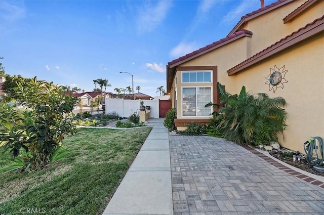 view of home's exterior with a patio, a tile roof, fence, a yard, and stucco siding