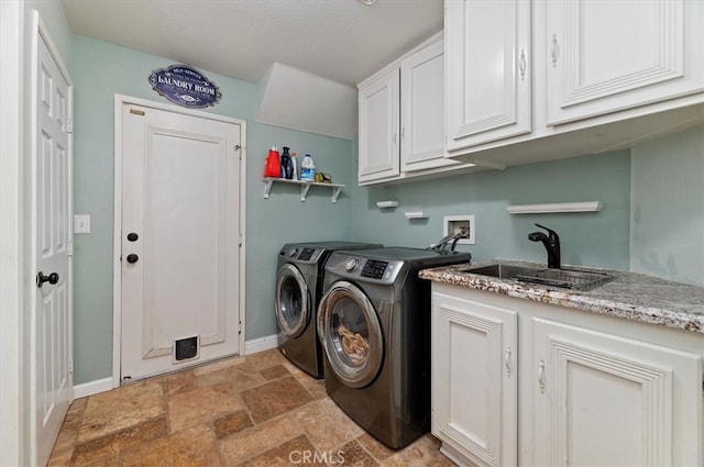 laundry area with cabinet space, baseboards, stone finish flooring, washing machine and dryer, and a sink