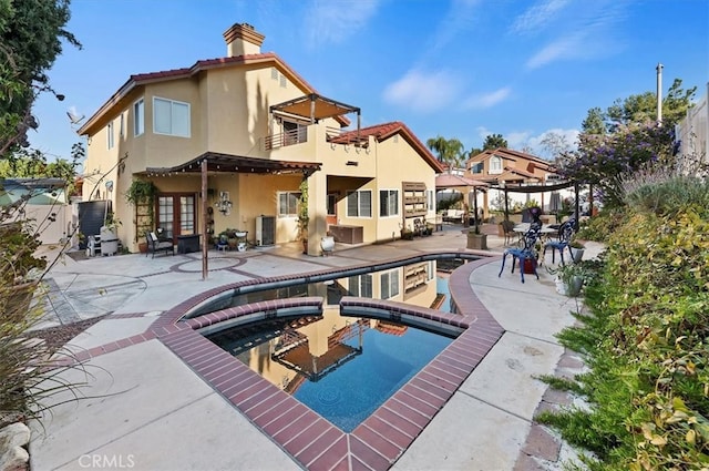 rear view of property featuring an in ground hot tub, a chimney, a patio area, and stucco siding