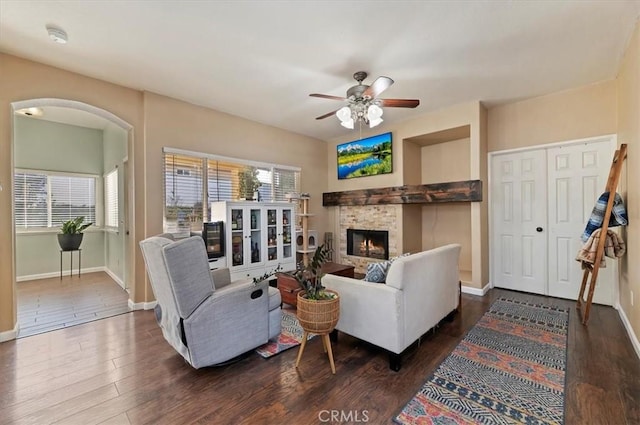 living area featuring a stone fireplace, wood finished floors, a ceiling fan, and baseboards